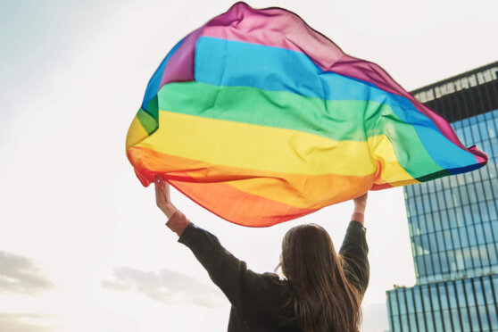 Silhouette of person holding flying rainbow flag